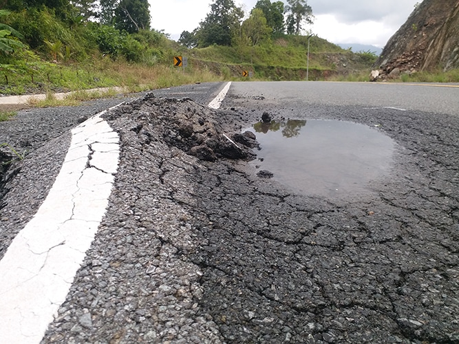 Cracked asphalt and rutting along a road edge with standing water